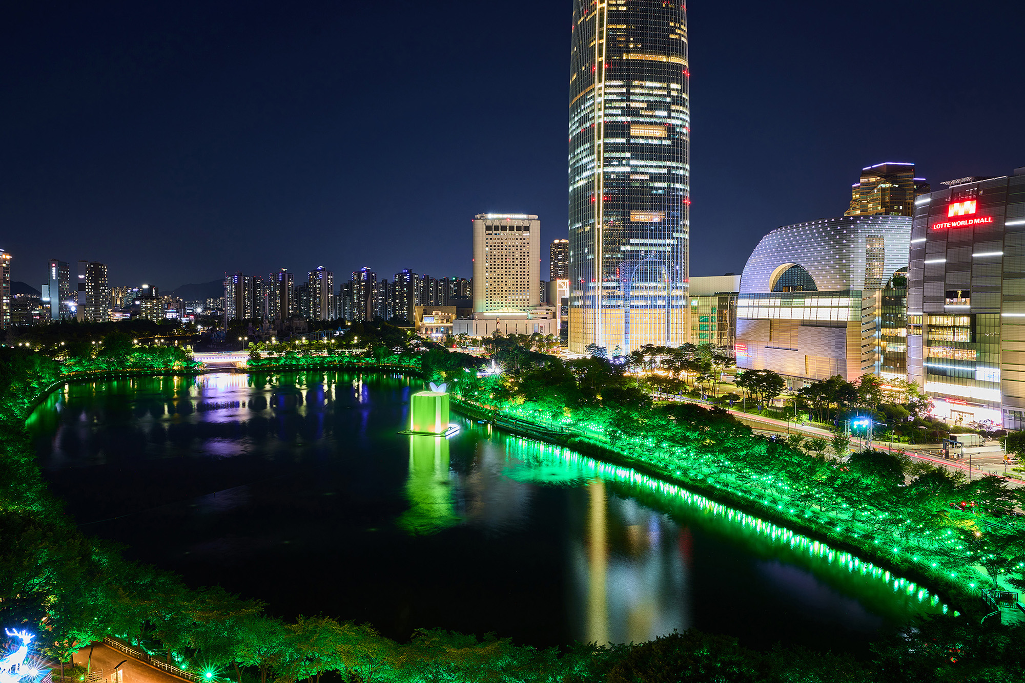 ロッテワールドタワーを背に緑色にライトアップされた夜の石村湖